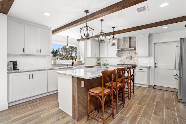 kitchen featuring light stone countertops, stainless steel fridge, wall chimney range hood, white cabinets, and a center island