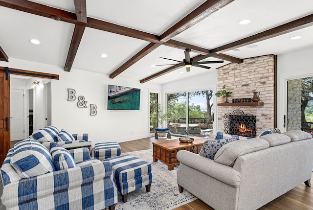 living room with hardwood / wood-style floors, lofted ceiling with beams, ceiling fan, a barn door, and a large fireplace