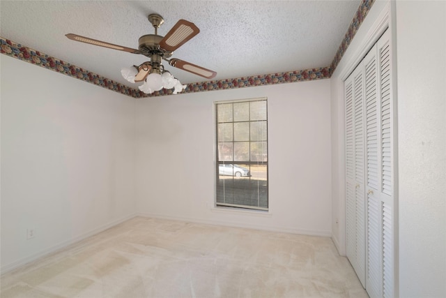 unfurnished bedroom featuring a textured ceiling, light colored carpet, ceiling fan, and a closet