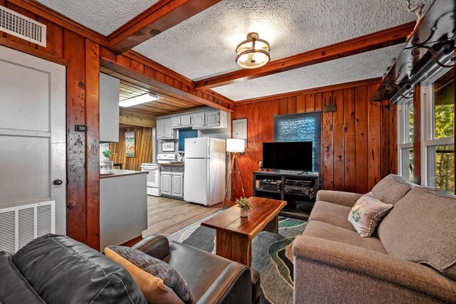 living room featuring light wood-type flooring, a textured ceiling, beamed ceiling, a wood stove, and wood walls