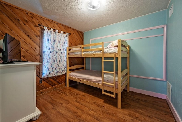 bedroom featuring hardwood / wood-style floors, a textured ceiling, and wooden walls