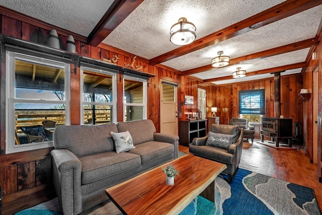 living room with wood walls, beamed ceiling, wood-type flooring, a wood stove, and a textured ceiling