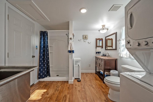 bathroom with hardwood / wood-style floors, stacked washer and dryer, vanity, toilet, and a shower with curtain