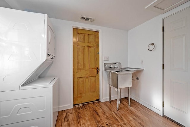 clothes washing area with light hardwood / wood-style floors and stacked washer / dryer