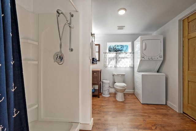 bathroom with hardwood / wood-style flooring, stacked washer / dryer, toilet, and a shower