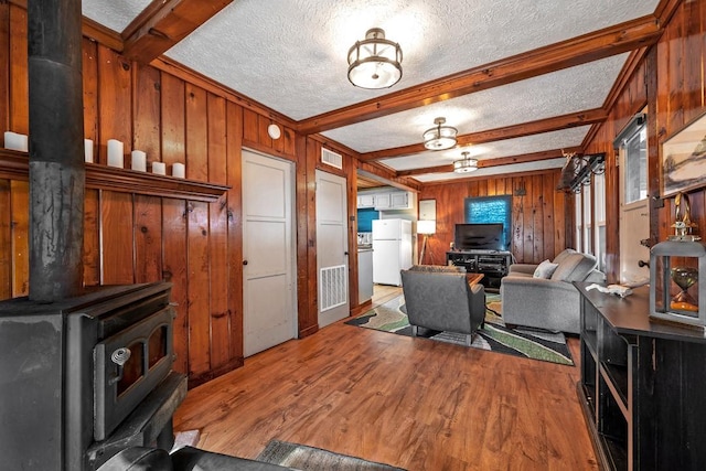 living room featuring a wood stove, wood walls, a textured ceiling, beamed ceiling, and light wood-type flooring