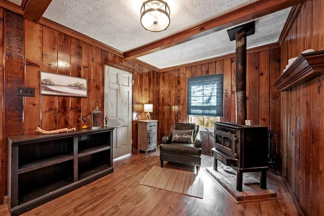 sitting room featuring beam ceiling, a wood stove, a textured ceiling, and light wood-type flooring