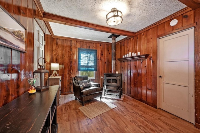 sitting room with a textured ceiling, a wood stove, wooden walls, beam ceiling, and hardwood / wood-style floors