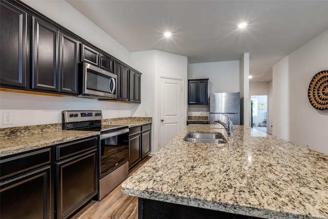 kitchen with light stone countertops, sink, a center island with sink, and appliances with stainless steel finishes