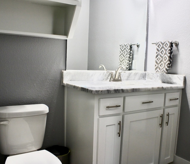 bathroom featuring vanity, a textured wall, and toilet