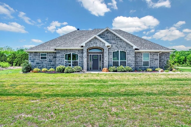 view of front facade featuring a front lawn, roof with shingles, and stone siding