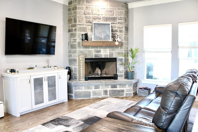 living room with light hardwood / wood-style floors, a stone fireplace, and ornamental molding