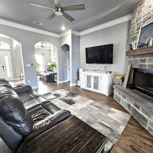 living room with ceiling fan, hardwood / wood-style floors, a textured ceiling, a fireplace, and ornamental molding