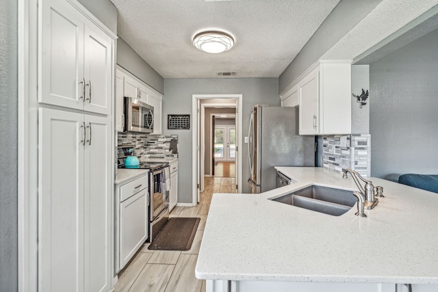 kitchen with sink, kitchen peninsula, decorative backsplash, white cabinetry, and stainless steel appliances