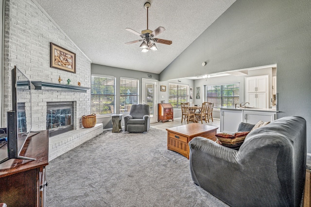 living room with high vaulted ceiling, a brick fireplace, ceiling fan, a textured ceiling, and light colored carpet