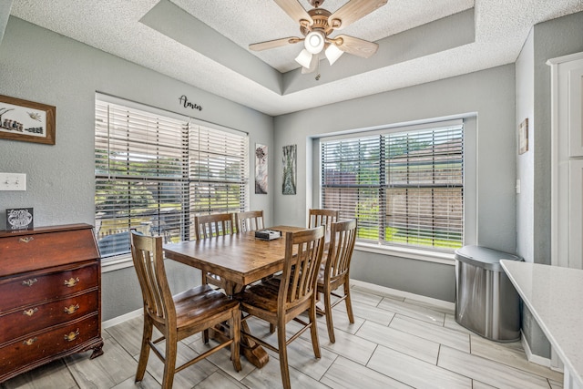 dining area with ceiling fan, a textured ceiling, and a tray ceiling