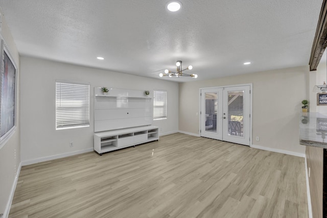 unfurnished living room featuring french doors, light hardwood / wood-style floors, a textured ceiling, and a notable chandelier