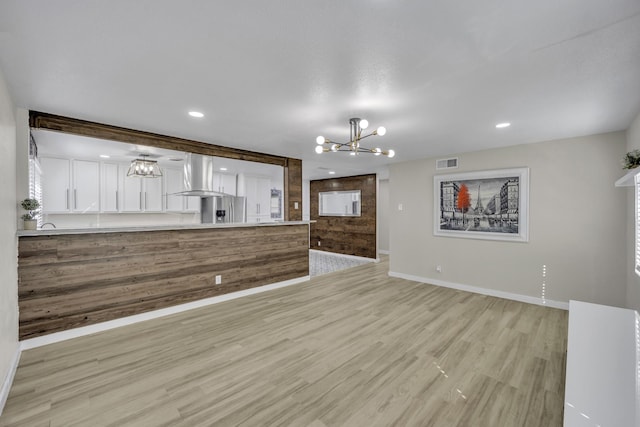 kitchen with wall chimney range hood, an inviting chandelier, stainless steel refrigerator with ice dispenser, light hardwood / wood-style floors, and white cabinets