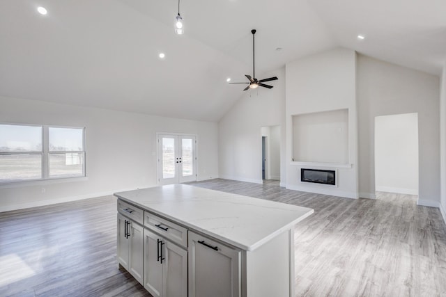 kitchen with hanging light fixtures, ceiling fan, light wood-type flooring, light stone countertops, and a kitchen island