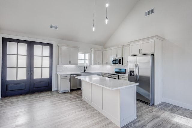 kitchen with high vaulted ceiling, french doors, white cabinets, appliances with stainless steel finishes, and a kitchen island