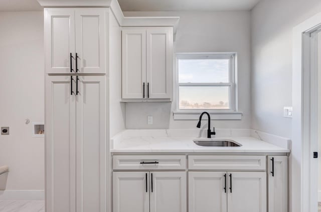 kitchen featuring white cabinets, light stone countertops, and sink