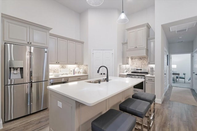 kitchen featuring a towering ceiling, an island with sink, sink, a kitchen breakfast bar, and stainless steel appliances