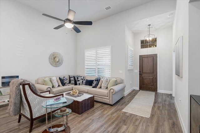 living room with hardwood / wood-style flooring, ceiling fan with notable chandelier, and a towering ceiling