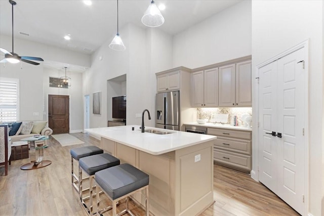 kitchen with sink, a breakfast bar area, stainless steel refrigerator with ice dispenser, a center island with sink, and decorative backsplash