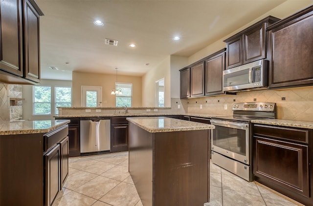 kitchen featuring kitchen peninsula, stainless steel appliances, sink, light tile patterned floors, and decorative light fixtures