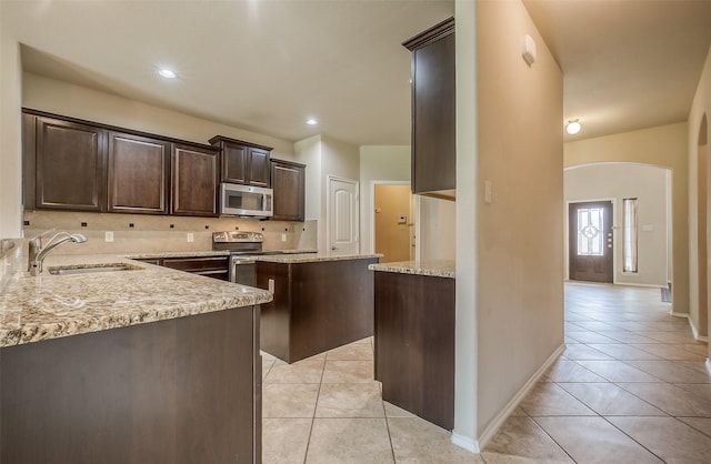 kitchen featuring light stone countertops, sink, a center island, stainless steel appliances, and light tile patterned flooring