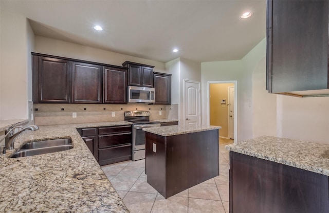 kitchen with sink, light stone counters, dark brown cabinets, a kitchen island, and appliances with stainless steel finishes