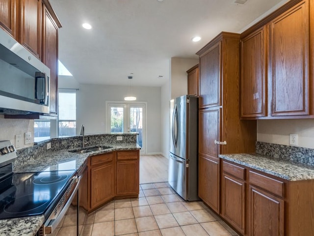 kitchen with pendant lighting, dark stone counters, sink, light tile patterned floors, and stainless steel appliances