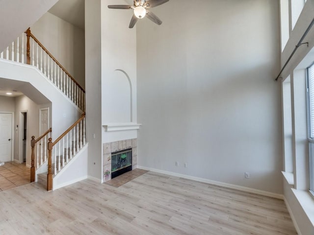 unfurnished living room with a fireplace, a towering ceiling, light hardwood / wood-style floors, and ceiling fan