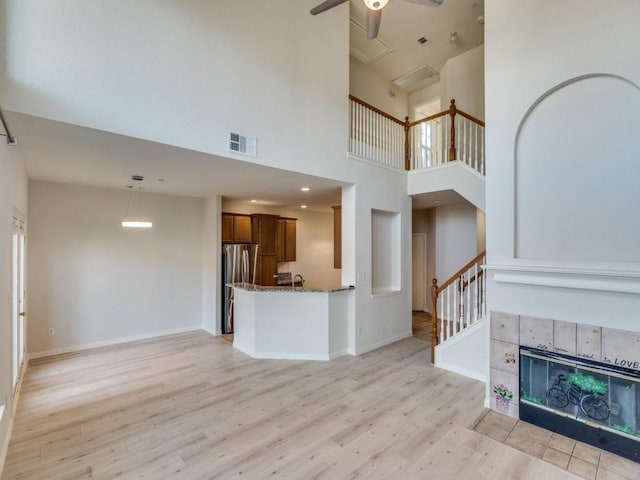 unfurnished living room featuring a fireplace, a high ceiling, light hardwood / wood-style flooring, and ceiling fan