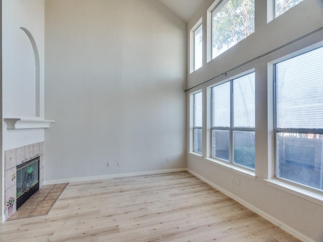 unfurnished living room featuring a high ceiling, a tile fireplace, and light hardwood / wood-style flooring