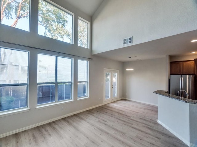 unfurnished living room featuring a towering ceiling, light wood-type flooring, and plenty of natural light