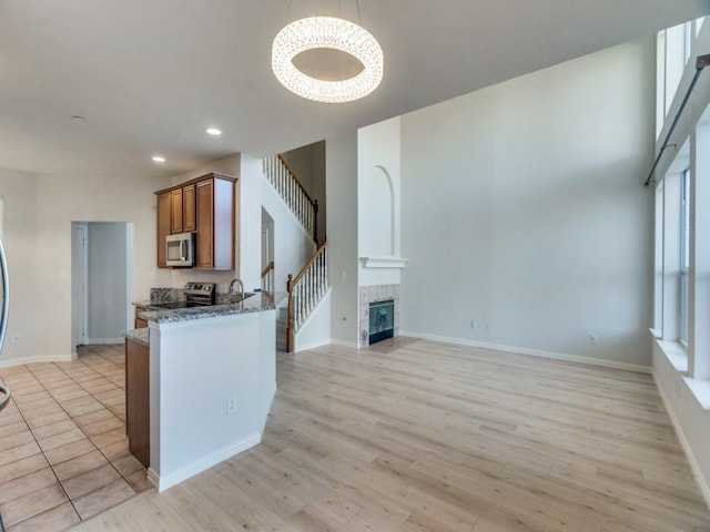 kitchen with stainless steel appliances, sink, decorative light fixtures, light hardwood / wood-style floors, and a tiled fireplace