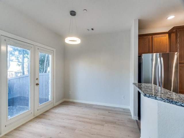 kitchen featuring french doors, hanging light fixtures, stainless steel fridge, dark stone counters, and light wood-type flooring