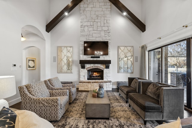 living room with high vaulted ceiling, dark hardwood / wood-style floors, beamed ceiling, and a stone fireplace