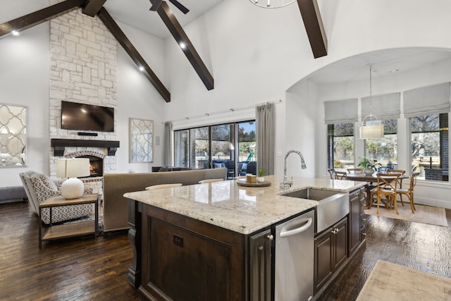 kitchen featuring sink, a fireplace, dark brown cabinetry, a kitchen island with sink, and beam ceiling