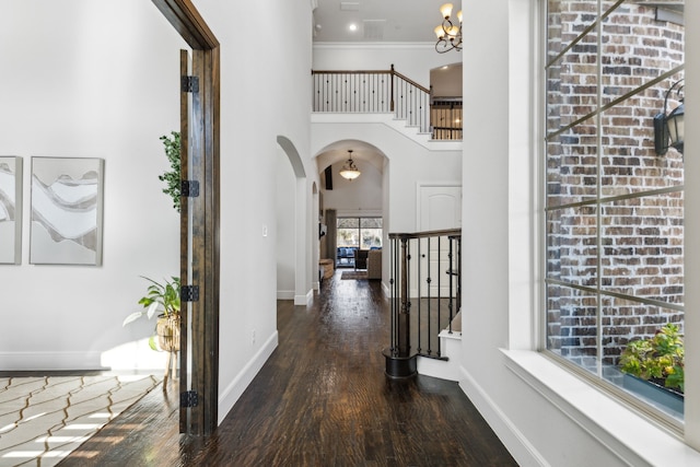 hall featuring a high ceiling, a chandelier, crown molding, and dark wood-type flooring