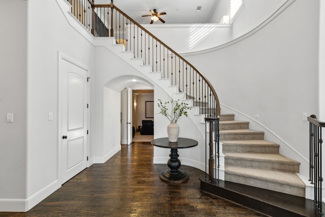 staircase with a towering ceiling, ceiling fan, and hardwood / wood-style floors