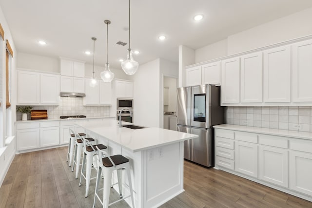 kitchen with white cabinets, stainless steel appliances, washing machine and dryer, and a center island with sink