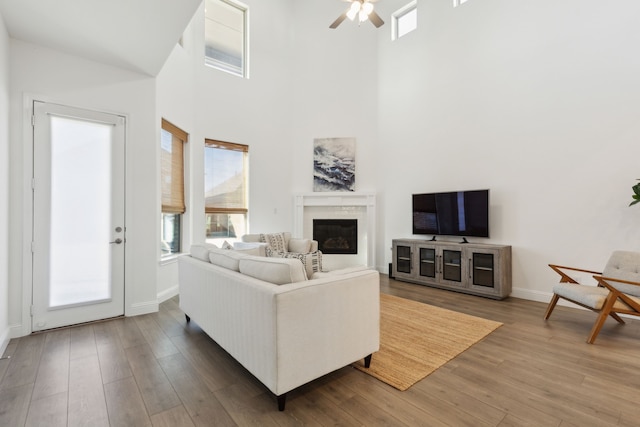 living room with a high ceiling, a premium fireplace, ceiling fan, and wood-type flooring