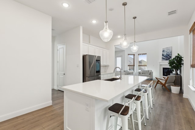 kitchen featuring sink, white cabinetry, an island with sink, stainless steel refrigerator, and pendant lighting