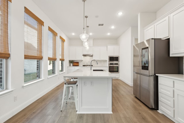 kitchen with stainless steel appliances, white cabinets, decorative light fixtures, and an island with sink