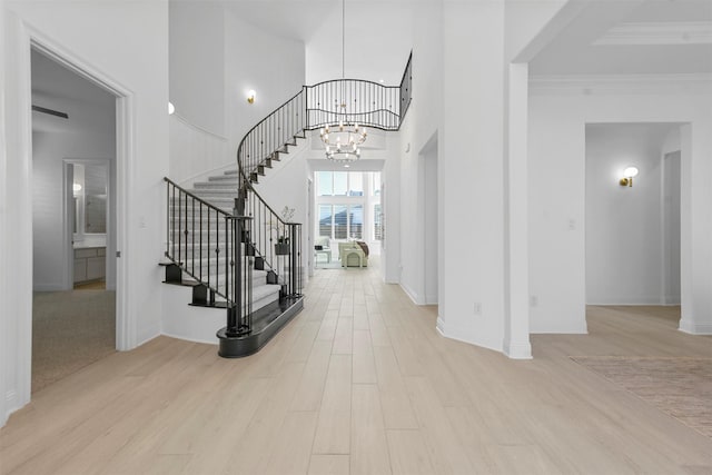 foyer entrance featuring ornamental molding, light wood-type flooring, and a notable chandelier