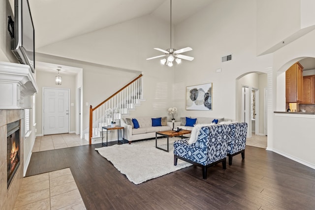 living room featuring ceiling fan, high vaulted ceiling, light hardwood / wood-style floors, and a tile fireplace