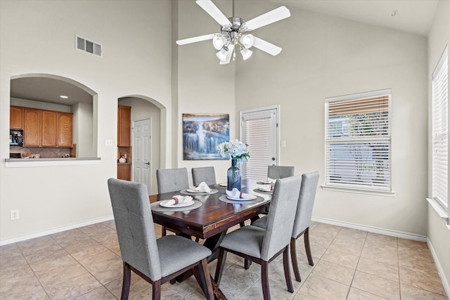 tiled dining space with ceiling fan and a high ceiling