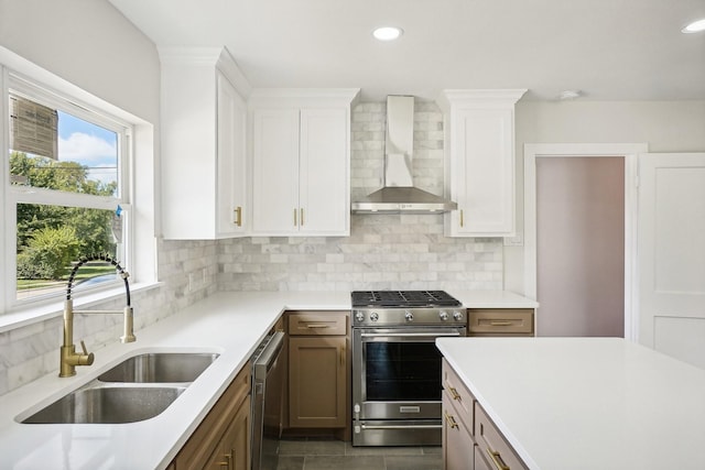 kitchen featuring backsplash, stainless steel appliances, sink, wall chimney range hood, and white cabinetry